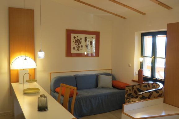 Schlafcouch FeWo am Zwenkauer See Gemütlicher Wohnraum mit Sofa, Tisch und Kunstwerk an der Wand. Helle Beleuchtung.