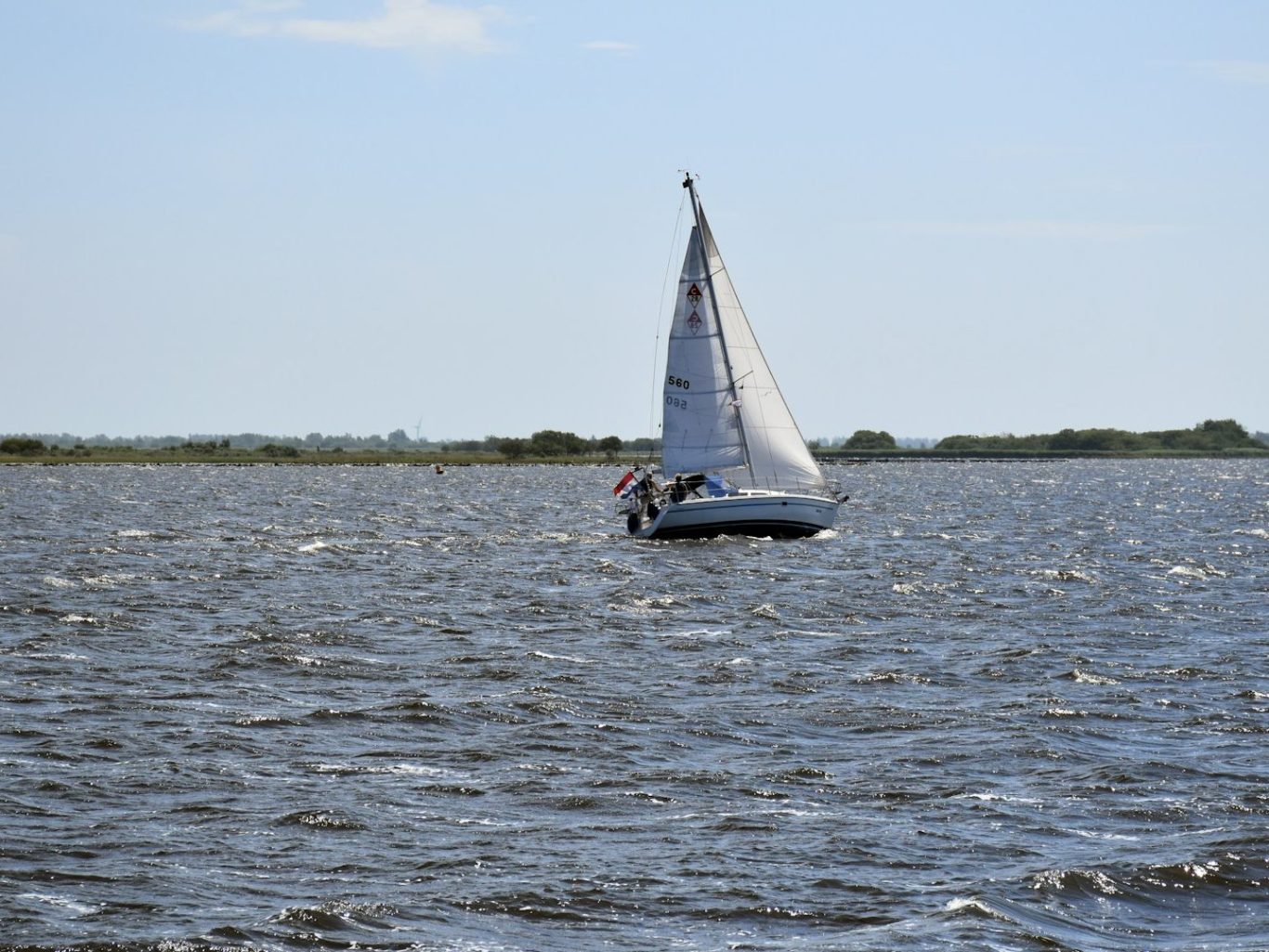 Mehr erfahren auf www.zwenkauer-see.com/erleben... Segelboot auf einem ruhigen Gewässer, umgeben von grüner Landschaft im Hintergrund.
