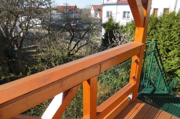 Blick vom Balkon - FeWo am Zwenkauer See Holzgeländer mit Blick auf einen Garten und Wohngebäude im Hintergrund.