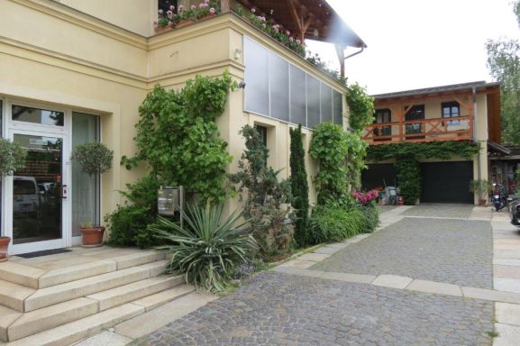 Einfahrt und Parkplatz - FeWo am Zwenkauer See Eingang mit Pflanzen, Treppen und einem Gebäude im Hintergrund.