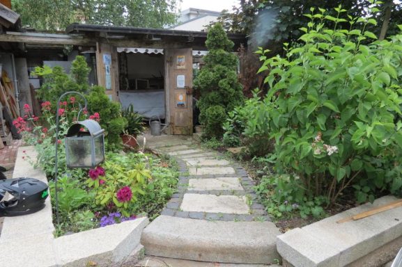 Blick in den Garten - FeWo am Zwenkauer See Ein Gartenweg mit Blumenbeeten und einem kleinen Schuppen im Hintergrund.