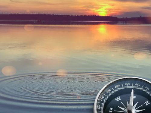 Mehr erfahren auf www.zwenkauer-see.com... Smartphone mit Kompassanzeige vor einer entspannenden Seelandschaft bei Sonnenuntergang.