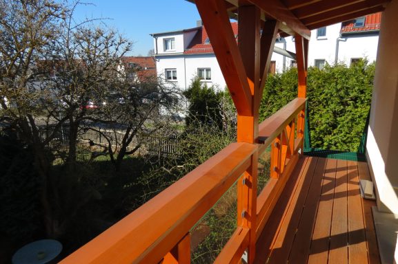 Perspektive vom Balkon - Ferienwohnung am Zwenkauer See Balkon mit orangefarbener Brüstung, Blick auf einen Garten und umliegende Gebäude.